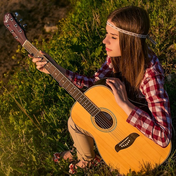 young woman playing a guitar setting in the grass